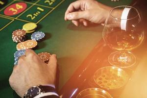 Mens spelen roulette in casino. dichtbij omhoog van mannetje handen met een glas van cognac en chips. foto
