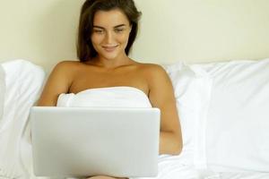 vrouw aan het liegen Aan de bed en gebruik makend van laptop pc foto