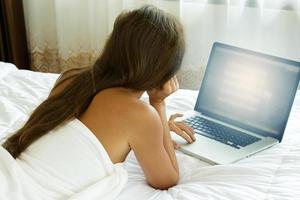 vrouw aan het liegen Aan de bed en gebruik makend van laptop pc foto