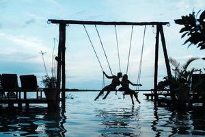 silhouet van paar Aan schommels welke is bovenstaand de water foto