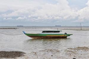 klein groen rivier- houten motor boot voor visvangst en vervoeren gebonden omhoog Bij de Ondiep zee. foto