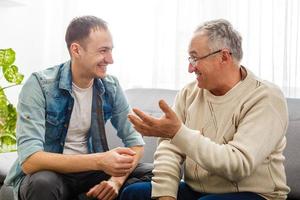 glimlachen gegroeid zoon zitten Aan bankstel kom tot rust met senior vader praten sharing gedachten op zoek in ogen, gelukkig millennial Mens rust uit Aan sofa spreken met ouderen vader genieten vrije tijd familie weekend Bij huis. foto