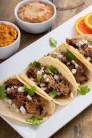 varkensvlees carnitas taco's met ui en koriander geserveerd met rijst- en opnieuw gebakken bonen foto