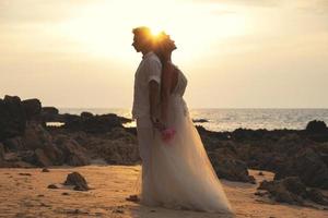 jong getrouwd paar in omhelzing is vieren hun bruiloft Aan de strand foto