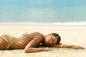 vrouw is aan het liegen Aan de strand onder palm blad foto