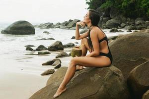 vrouw zittend Aan de rotsachtig strand foto