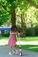 weinig zwart meisje met een trap scooter in een stad park foto