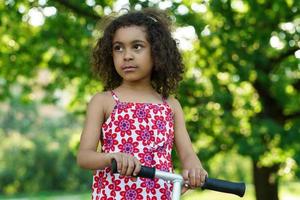 weinig zwart meisje met een trap scooter in een stad park foto