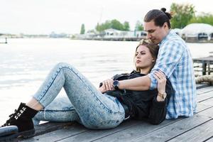 jong sensueel en liefhebbend paar zittend Aan een pier naast een rivier- foto