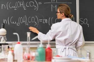 leraar uitleggen hoe naar lezen een chemisch vergelijking Aan een schoolbord gedurende een chemie les foto