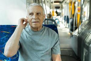 ouderen Mens is gebruik makend van draadloze oordopjes gedurende rijden in openbaar vervoer foto