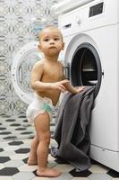 schattig baby jongen naast de het wassen machine foto