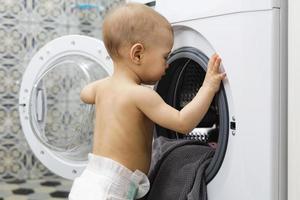 schattig baby jongen is op zoek binnen de het wassen machine foto