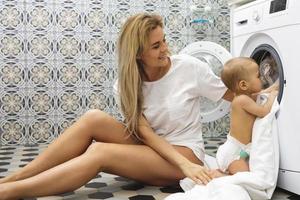 moeder en haar weinig baby zoon zijn bezig met laden het wassen machine foto