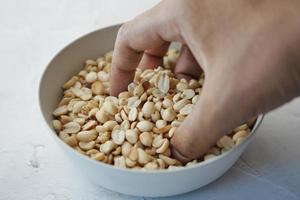 hand- plukken verwerkt pinda's in een kom Aan tafel foto