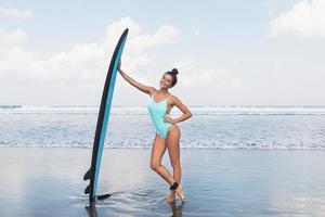 jong vrouw vervelend gestreept zwempak met surfboard Aan de strand foto