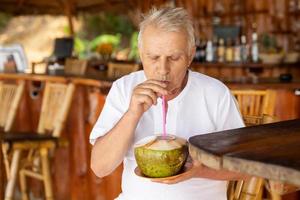 gelukkig senior Mens is drinken een kokosnoot water in de strand bar foto