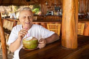 gelukkig senior Mens is drinken een kokosnoot water in de strand bar foto