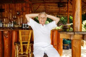 gelukkig senior Mens is drinken een kokosnoot water in de strand bar foto