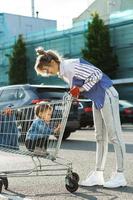 jong moeder en haar schattig weinig zoon zijn hebben pret met boodschappen doen kar foto