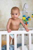 schattig baby eerste tijd staand omhoog in zijn kinderbed foto