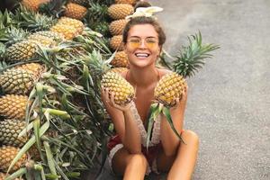 jong en gelukkig vrouw met een stapel van ananas Aan de lokaal Thais markt foto