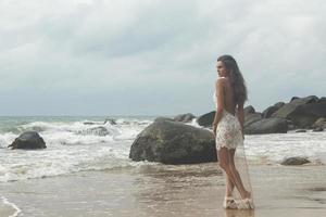 jong vrouw vervelend mooi wit jurk is poseren Aan de strand foto