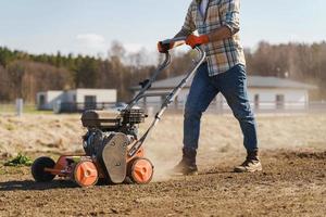 Mens gebruik makend van beluchter machine naar insnijding en beluchting van gazon of weide foto