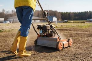 vrouw dorpeling is gebruik makend van beluchter machine naar insnijding en beluchting van gazon of weide foto