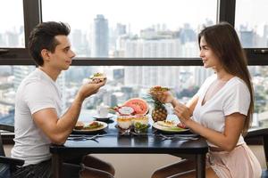 gelukkig paar aan het eten gezond ontbijt in modern appartement met groot ramen en stad visie foto