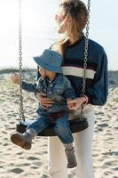 jong moeder en haar zoon Aan schommel zijn op zoek weg Bij de strand. foto