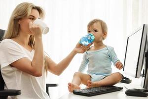 jong freelancer moeder drankjes koffie en haar zoon drankjes water Bij huis kantoor. foto