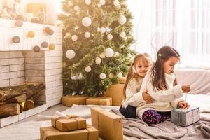 kinderen weinig zussen houden cadeaus dozen interieur achtergrond. wat een Super goed verrassing. klein schattig meisjes ontvangen vakantie geschenken. het beste speelgoed en Kerstmis geschenken. kinderen vrienden opgewonden uitpakken hun geschenken. foto