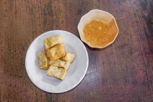 top visie Chinese tussendoortje en vegetarisch voedsel gebakken tofu Aan wit keramisch bord en pinda zoet en verzuren pittig saus Aan klein keramisch kom en houten tafel achtergrond. foto