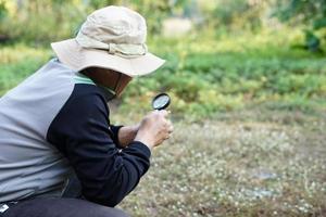 Mens ontdekkingsreiziger houdt vergroten glas naar onderzoeken klein planten in tuin. concept, onderzoeken, ontdekken, Onderzoek natuur of biologisch organismen. studie over milieu en planten. foto