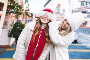 jong gelukkig Dames vrienden met gekruld haar- in rood hebben pret in winter straat versierd met lichten foto