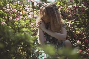 geabsorbeerd in gedachte meisje omringd door struiken met roze bloemen toneel- fotografie foto