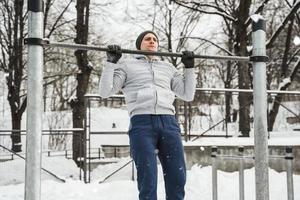 atletisch Mens aan het doen optrekken Aan horizontaal bar gedurende zijn buitenshuis winter training foto