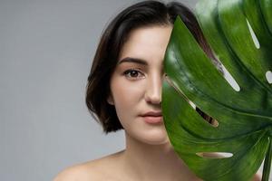 portret van jong mooi brunette vrouw met een monstera deliciosa tropisch blad foto
