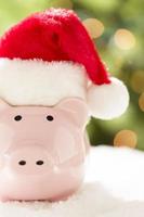 roze varkentje bank met de kerstman hoed Aan sneeuwvlokken foto
