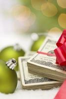 stack van honderd dollar rekeningen met boog in de buurt Kerstmis ornamenten foto