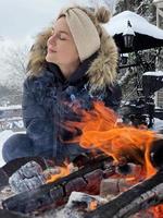 jong vrouw opwarming omhoog door de brand pit gedurende verkoudheid winter dag foto