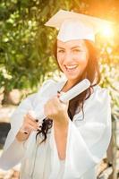 afstuderen gemengd ras meisje in pet en japon met diploma foto