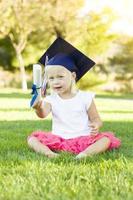weinig meisje in gras vervelend diploma uitreiking pet Holding diploma met lint foto