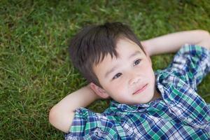 attent gemengd ras Chinese en Kaukasisch jong jongen ontspannende Aan zijn terug buiten Aan de gras foto