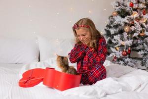 een gelukkig weinig meisje ontvangen een schattig katje net zo een geschenk voor de nieuw jaar. Kerstmis ochtend. hoog kwaliteit foto