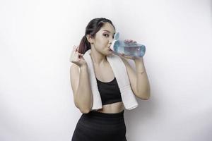 sportief Aziatisch vrouw poseren met een handdoek Aan haar schouder en drinken van een fles van water, glimlachen en ontspannende na training foto