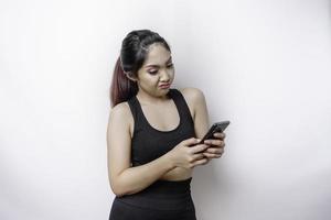 een ontevreden sportief Aziatisch vrouw looks ontevreden vervelend sportkleding geërgerd gezicht uitdrukkingen Holding haar telefoon foto