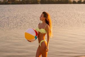 aanbiddelijk slank dame in zwempak met strand bal in de zee foto