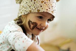 schattig weinig meisje eet chocola crème in wit keuken Bij huis foto